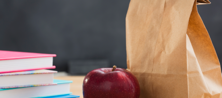 Brown lunch bag on desk with an apple and books