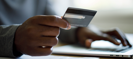 Handing holding a credit while typing on a laptop