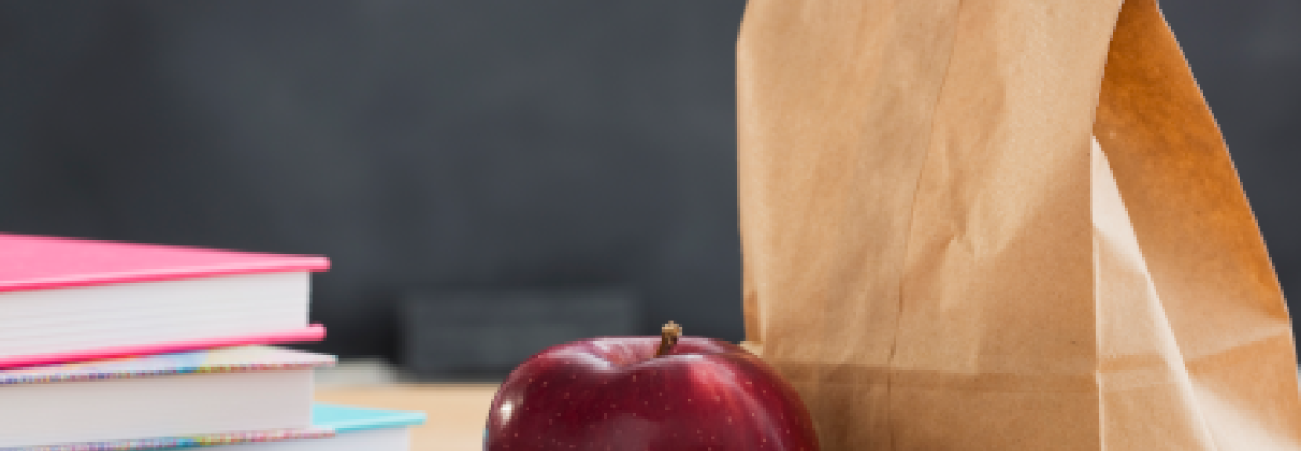 Brown lunch bag on desk with an apple and books