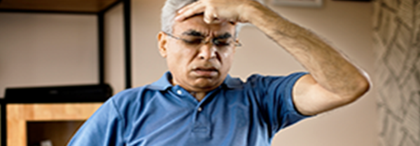 Senior man suffering from a headache with hand to head and anguished face.